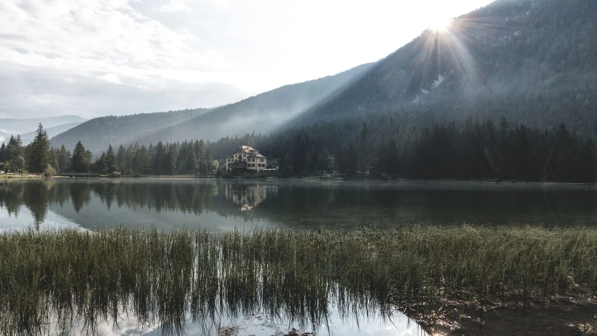 Peaceful lake view with house, mountains, and forest at sunrise. Tranquil and serene atmosphere.